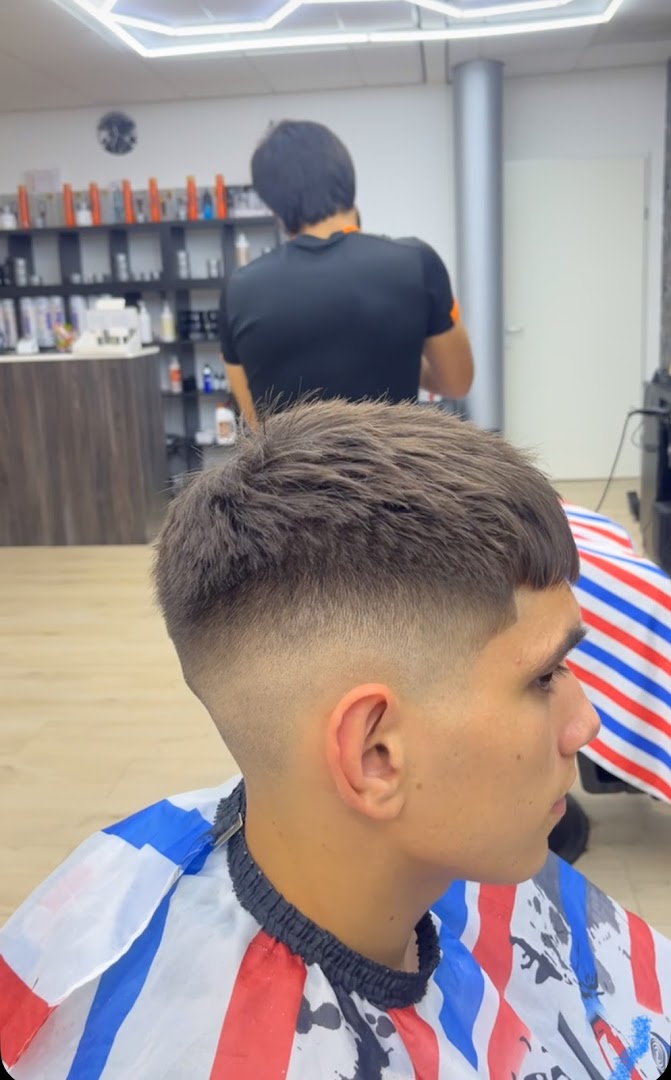 Een barbier van Barbershop Arshad aan het werk, met een klant in de stoel op de voorgrond en de hexagon-LED-verlichting en productschappen op de achtergrond
